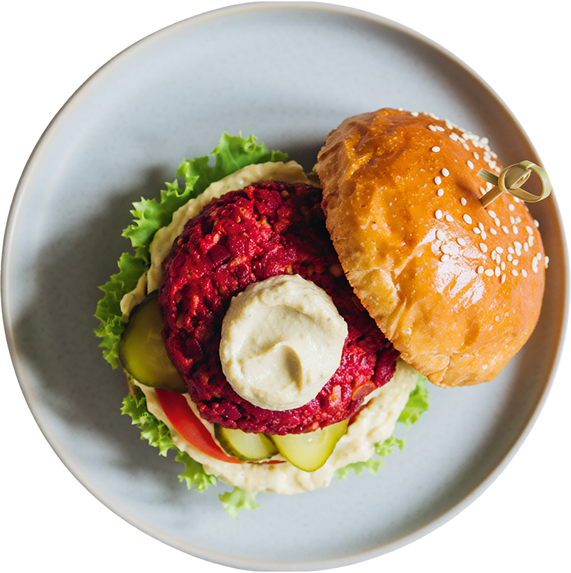 Vegetarischer Rote-Bete-Burger mit cremigem Hummus, Essiggurken und frischem Salat im Sesambrötchen.