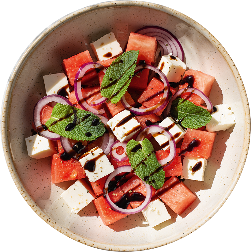 Wassermelonen-Feta-Salat mit frischer Minze, roten Zwiebeln und Balsamico-Dressing in einer Schüssel angerichtet.