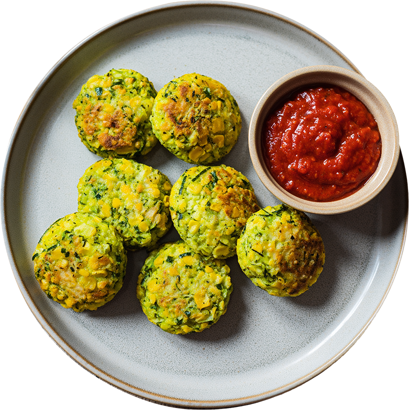 Goldbraune Mais-Zucchini-Bällchen mit frischem Tomatendip auf einem grauen Teller angerichtet.